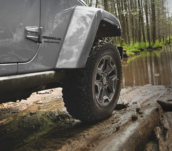 Close-up of Jeep Wrangler wheel as vehicle is being driven on muddy terrain.